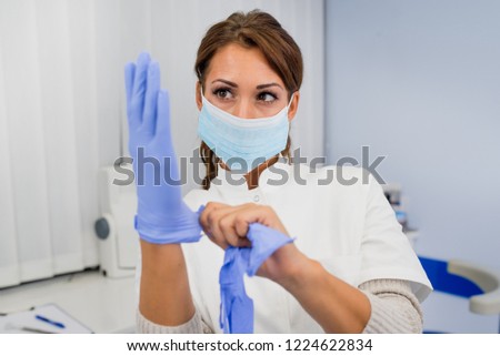 Close up of female doctor's hands putting on blue sterilized surgical gloves in the medical clinic
