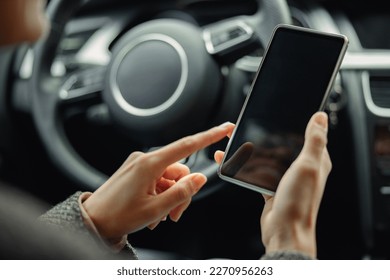 Close up of female driver hands is using phone while sitting behind steering wheel in own car