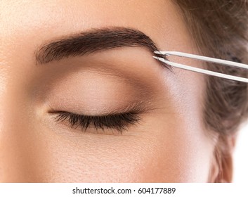 Close up of female face and eyebrow with tweezers