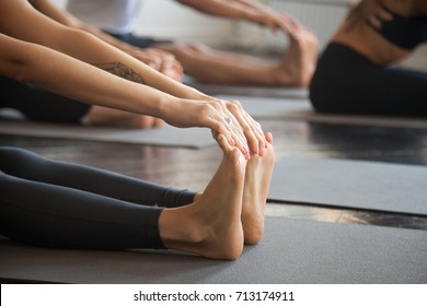 Close up of female feet, group of young sporty people practicing yoga lesson with instructor, sitting in paschimottanasana exercise, Seated forward bend pose, working out, studio, concept  - Powered by Shutterstock