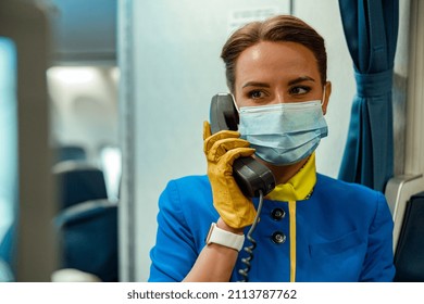 Close Up Of Female Flight Attendant In Protective Face Mask Having Phone Conversation In Aircraft Cabin