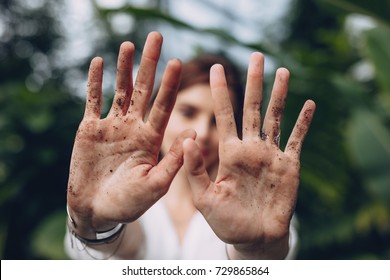 Close up of female gardener showing her dirty hands with soil and earth at greenhouse. Woman after garden work and landscaping in the plant nursery.