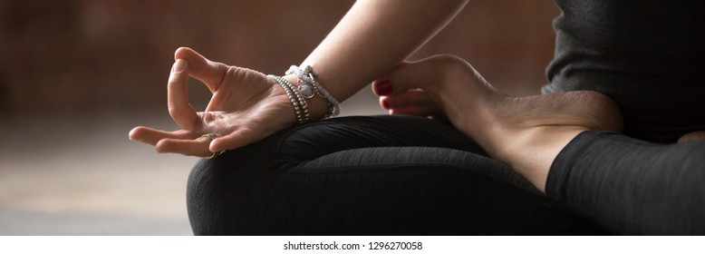 Close up female hand with bracelets fingers in Gyan mudra symbol of wisdom, girl wearing black activewear practice yoga sitting in lotus pose, banner for website header design with copy space for text