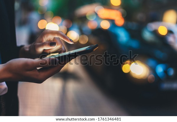 Close up female hand calling taxi with a\
smartphone app., businesswoman using cellphone with yellow taxi\
background in night\
street