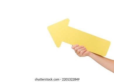 Close up of female hand holding big yellow paper arrow pointer on copy space for promotion content or design, posing isolated over white studio background wall. Business and strategic concept