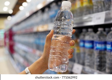 Close Up Female Hand Holding A Bottle Of Water Or Mineral Water In Grocery Store.