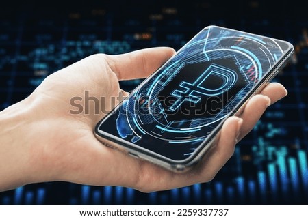 Close up of female hand holding cellphone with glowing blue ruble on dark background. Money, digital banking and finance concept