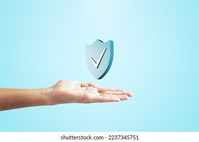 Close up of female hand holding creative antivirus shield icon on light blue background. Secure phone usage, protection and web safety concept