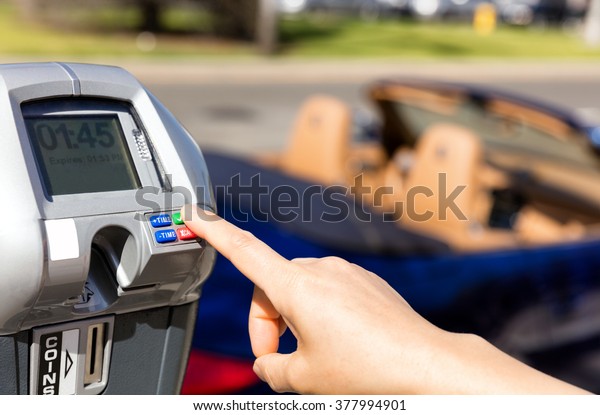 Close up of female hand, index finger,
selecting parking meter time outdoors on street. Selective focus on
tip of index finger and meter buttons.
