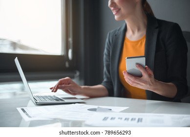 Close up female hand keeping phone while typing in modern laptop in office. Technology and job concept Foto Stock