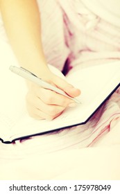 Close up of female hand making notes in calendar at bed. 
