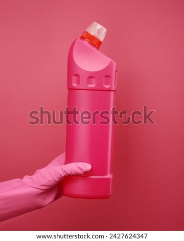 Close up of female hand in pink protective rubber glove holding plastic bottle against pink background