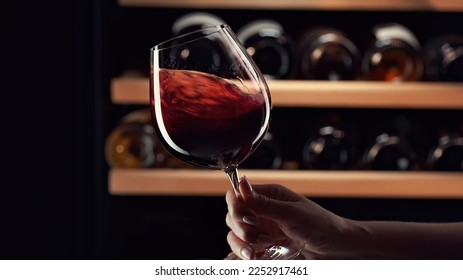 Cierra la mano femenina girando vino tinto en vaso de vino. Degustación de vinos, clasificación y bebida, botellas de fondo.