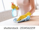 Close up female hand wear rubber latex protective yellow glove cleaning wooden kitchen countertop surface with soft microfiber blue rag. Housekeeping, professional products for cleaning home concept