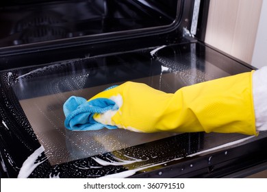 Close Up Of Female Hand With Yellow Protective Gloves Cleaning Oven Door