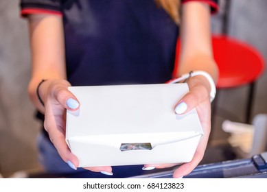 Close Up Female Hands Holding And Giving Take Out Food In White Paper Box Through The Window Of Issuing Orders. Selective Focus. Street Food Concept.