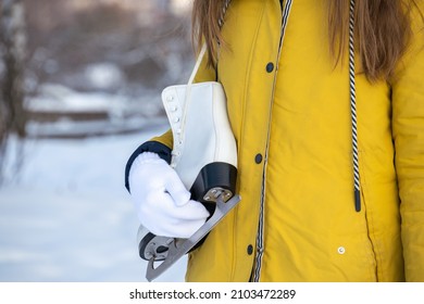 Close Up Of Female Hands Holding Ice Skates. Young Woman In Yellow Coat With Skates.