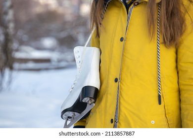 Close Up Of Female Hands Holding Ice Skates. Young Woman In Yellow Coat With Skates.