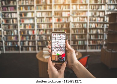 Close Up Female Hands Holding Mobile. She Taking Photo Of Table With Books In Library