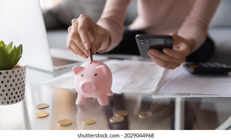 Close up female hands holding smartphone put euro coin into piggy bank, advanced modern tech user using of mobile budget tracking app for personal finances, family money management, e-banking concept