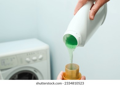 Close up of female hands pouring liquid laundry detergent into cap in the washing machine. Pour green washing liquid, wash machine blured in background. - Shutterstock ID 2334810523