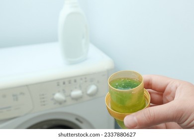 Close up of female hands pouring liquid laundry detergent into cap in the washing machine. Pour green washing liquid, wash machine blured in background. - Shutterstock ID 2337880627