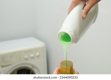 Close up of female hands pouring liquid laundry detergent into cap in the washing machine. Pour green washing liquid, wash machine blured in background. - Shutterstock ID 2344090233
