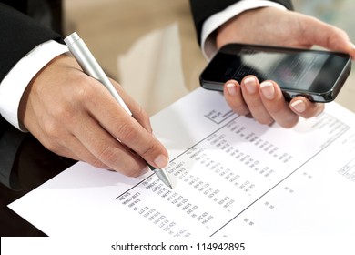 Close Up Of Female Hands Reviewing Accounting Documents With Smart Phone.