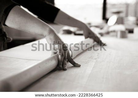 Close up of female hands working with rolling-pin for italian fresh pasta -  Female hands rolling  for fresh dough on the wooden table - concept of cooking and fresh homemade pasta - retro style