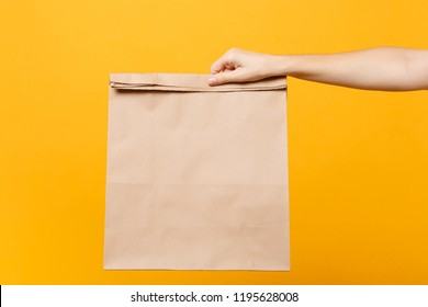 Close Up Female Hold In Hand Brown Clear Empty Blank Craft Paper Bag For Takeaway Isolated On Yellow Background. Packaging Template Mockup. Delivery Service Concept. Copy Space Advertising Area