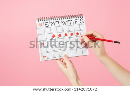 Close up female holds in hand red pencil, female periods calendar for checking menstruation days isolated on trending pink background. Medical healthcare gynecological concept. Copy space. Mock up.