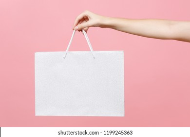Close up female holds in hand white clear empty blank craft paper gift bag for purchases after shopping isolated on pastel pink background. Packaging template mockup. Delivery concept advertising mock