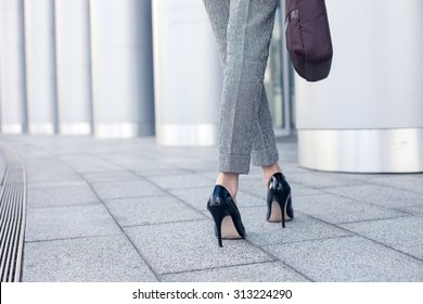 Close up of female legs of worker standing near her office. The woman is wearing formalwear and shoes on high heels. She is holding a handbag. Copy space in left side - Shutterstock ID 313224290