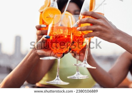 Close up of female and male hands holding elegant glasses with long stem of aperol and clink them. Making a celebratory toast with delicious citrus alcohol cocktails with slice of orange. Party.