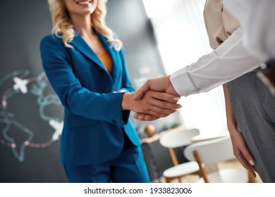 Close up of female manager and client handshaking after making a deal at the travel agency office. Tourism, travelling, business concept