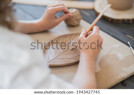 Close up of female potter holding stick and making ornament on earthenware. Clay master moulding clay product. Concept of ceramic art and hobby.