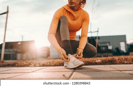 Close up of female runner kneeling and tying shoelace on the street on sunny day. - Powered by Shutterstock