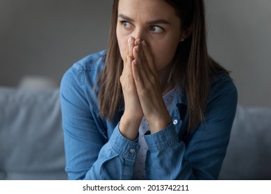 Close up female scared face sit on sofa with folded palms looks into distance feels horrified by bad awful news. Afraid of life difficulties, worrying about problem, hesitation, mistake, doubt concept - Shutterstock ID 2013742211