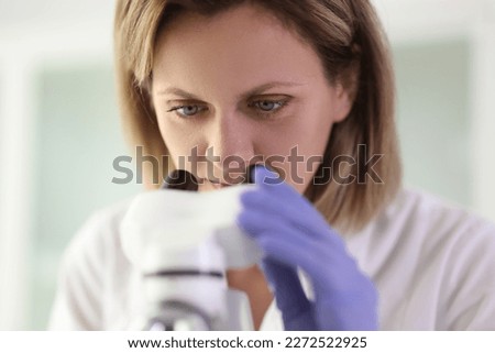 Close up of female scientist looks through microscope in research laboratory. Science and education concept.