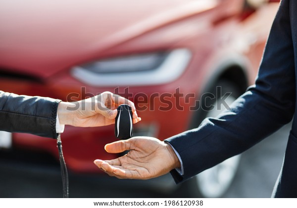 Close up of female seller presenting keys from red\
electric car to male customer. Blur background of luxury auto.\
Concept of successful\
deal.