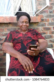   Close  up  of  a  female  senior  citizen  browsing cellphone  whilst  seated  on  outdoors  with  a  brick wall  behind.                             