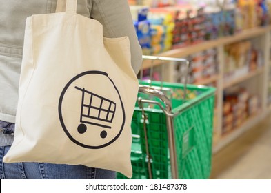 Close Up Of A Female Shopper With A Canvas Tote Bag Pushing A Shopping Cart Down The Isle Of A Specialty Grocery Store.