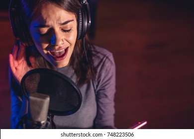 Close Up Of Female Singer Singing In A Microphone. Young Woman Music Artist Singing A Song In The Recording Studio.