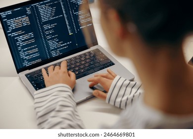 Close up of female software engineer writing code on laptop with screens setup in coworking