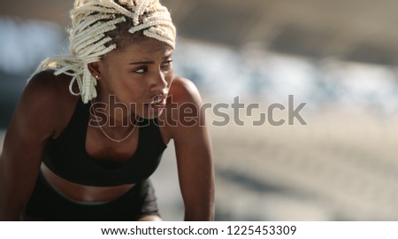 Close up of a female sprinter standing inside a stadium. Tired athlete relaxing bending forward.