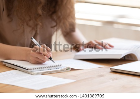 Close up of female student sit at table study using  handbook write in notebook doing research, motivated girl prepare for test or exam learning handwriting in workbook, making notes of important data
