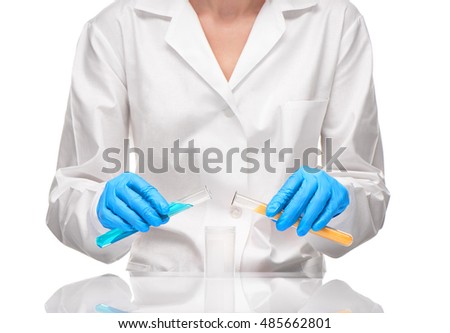 Close up of female in white gown and blue gloves holding transparent white glass test tubes and with yellow sorbent and blue liquid over measuring cup against white background