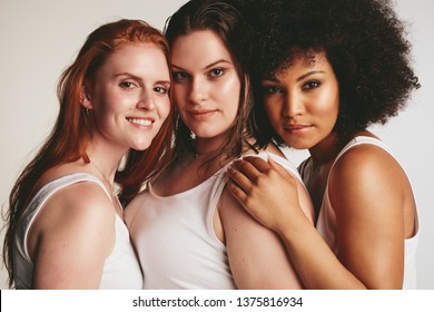 Close up of females of different size in white tank top staring at camera. Three diverse women friends against white background.