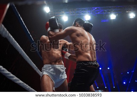 Close fight of two boxers in the ring of big sport arena full of light and spectators
