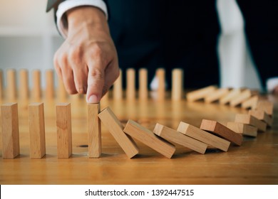 Close up finger businessman stopping wooden block from falling in the line of domino with risk concept. - Shutterstock ID 1392447515